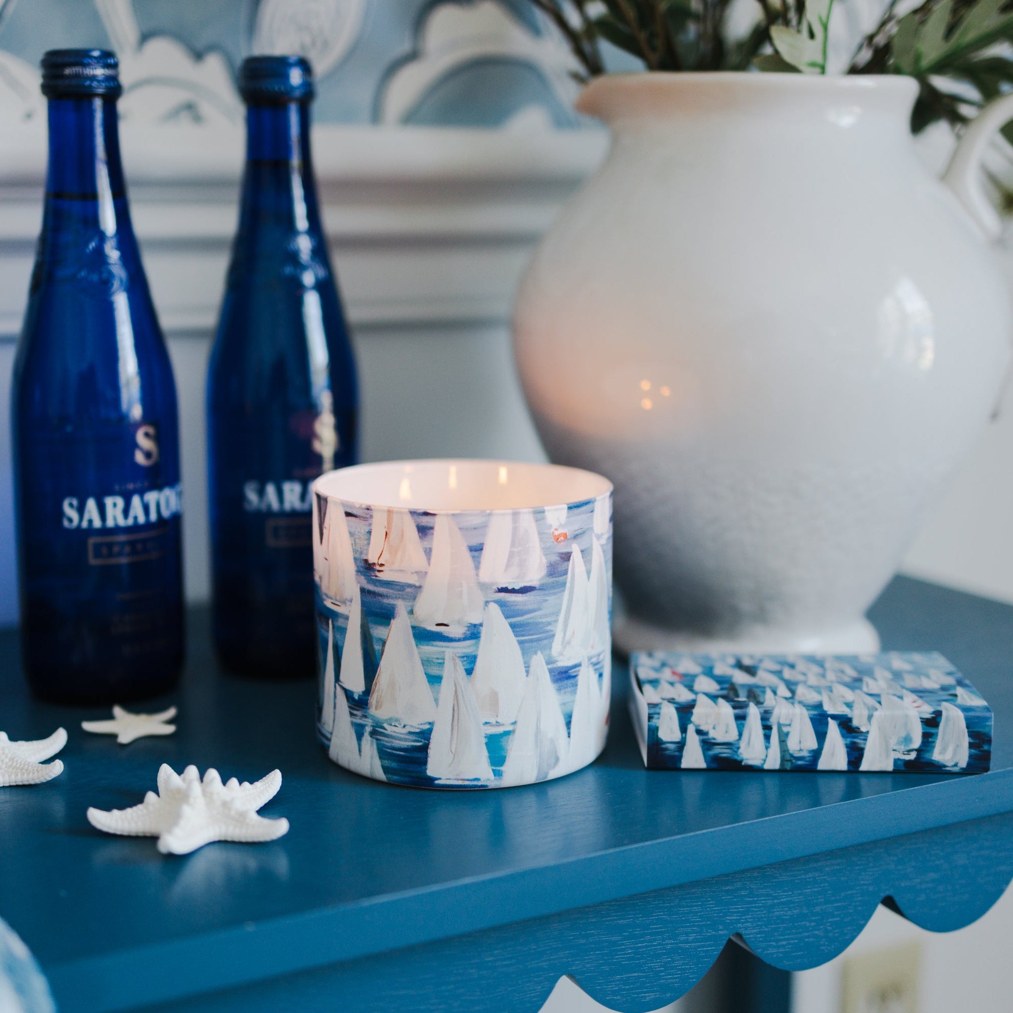 Three blue bottles on a blue surface with decorative sailboat candle and matching matchbox