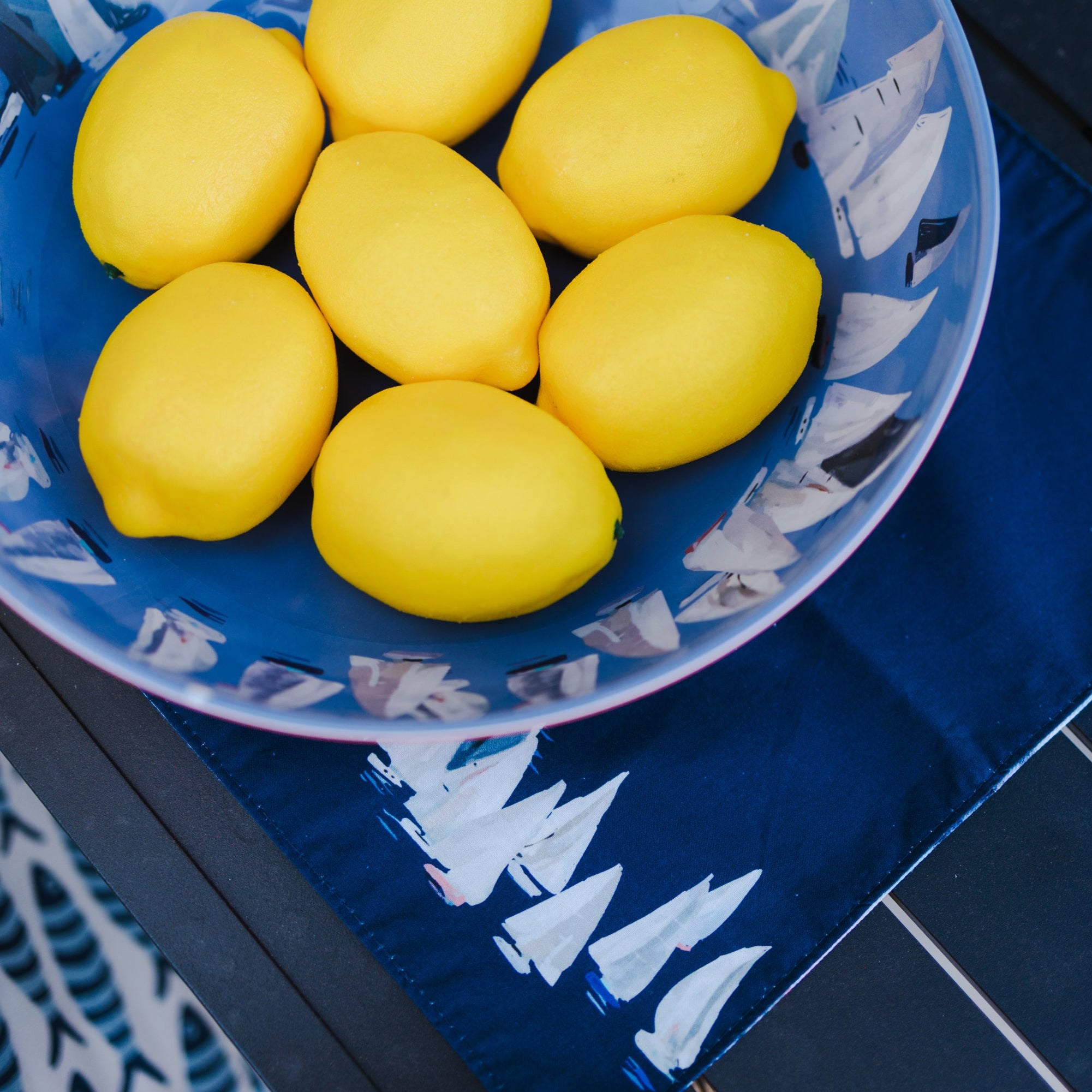 Blue plate with white boat pattern containing yellow lemons on a blue surface.