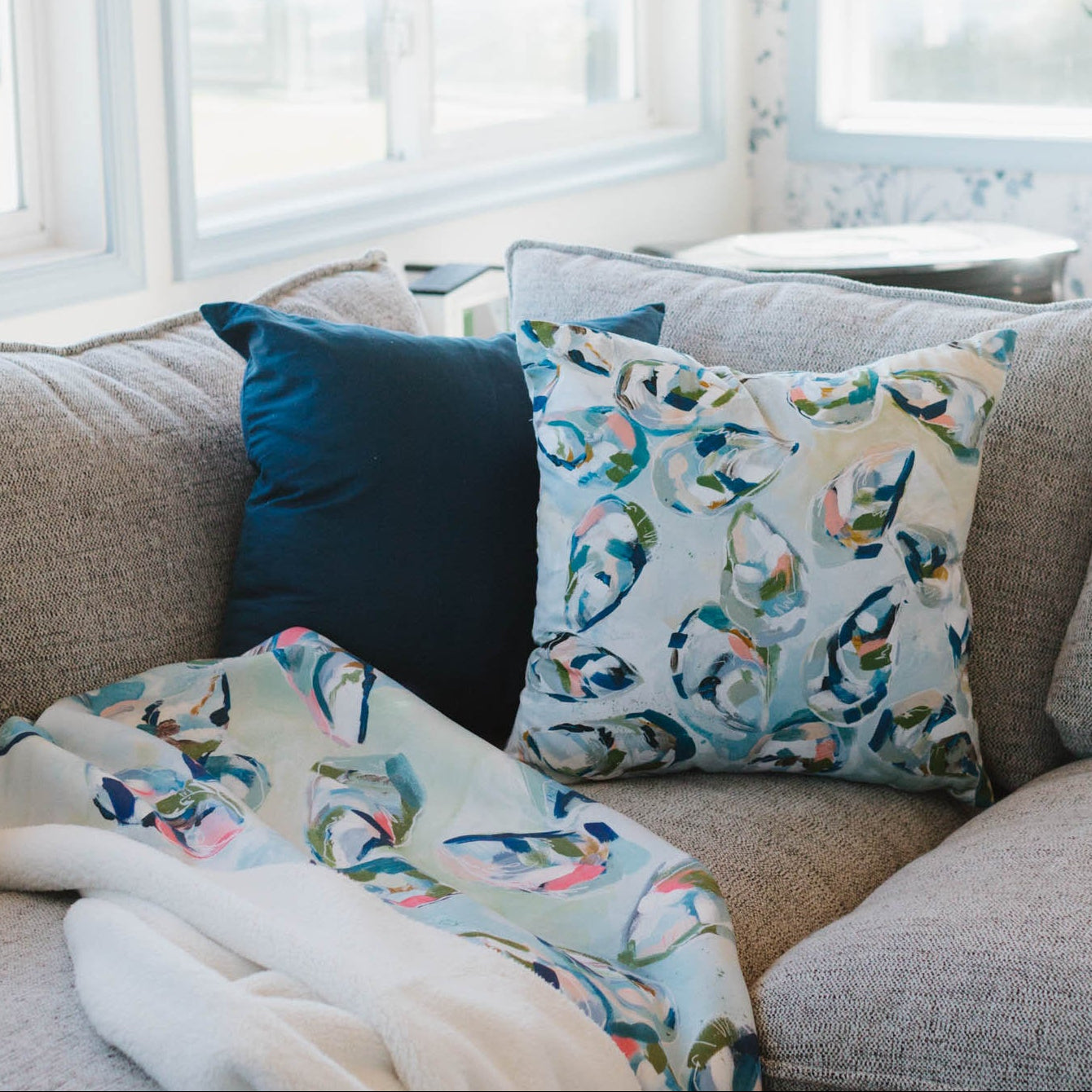 Gray sofa with patterned cushions and a blanket, next to a small table with popcorn and a bowl.