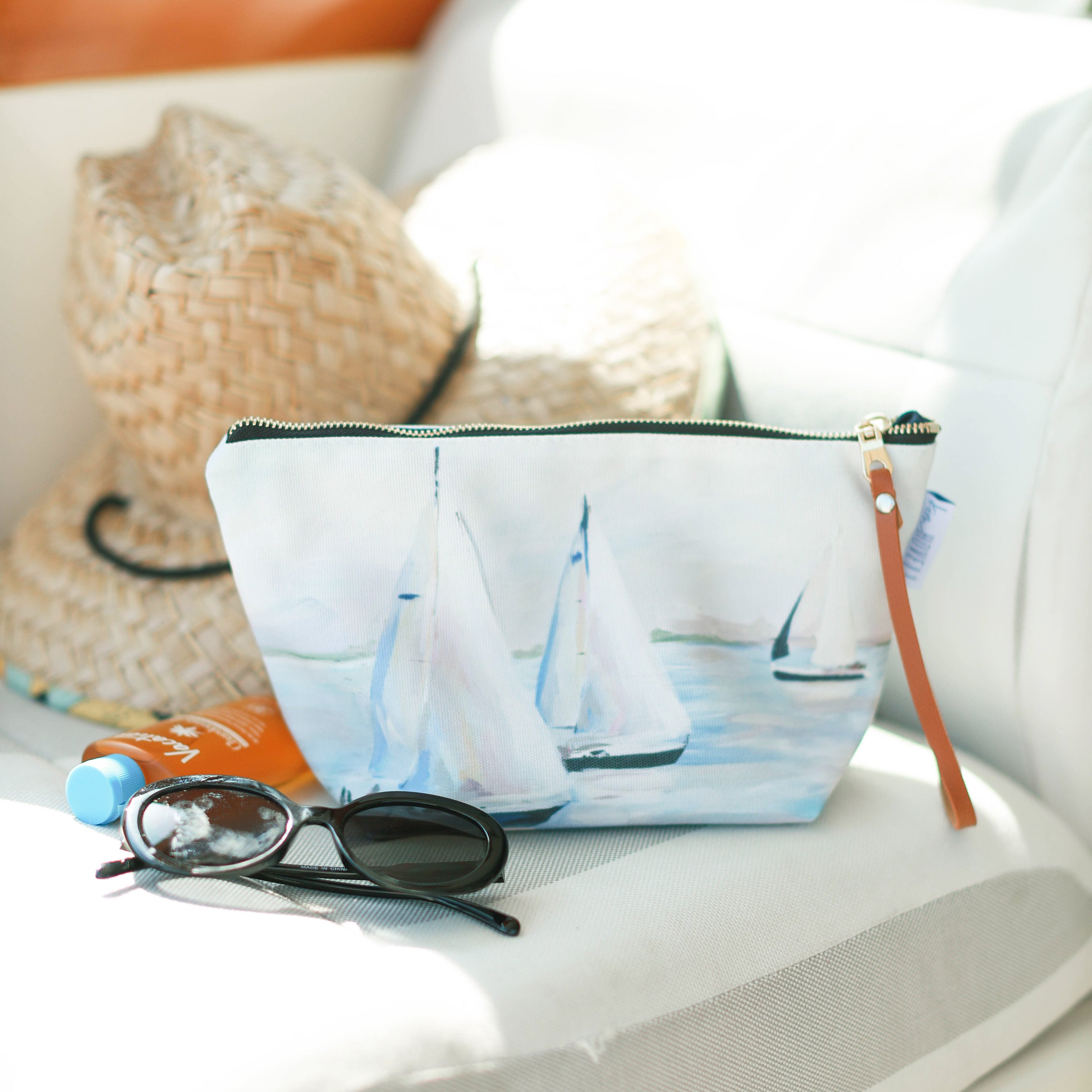 pouch with Kim Hovell sailboat design, sunglasses, and hat on boat seat