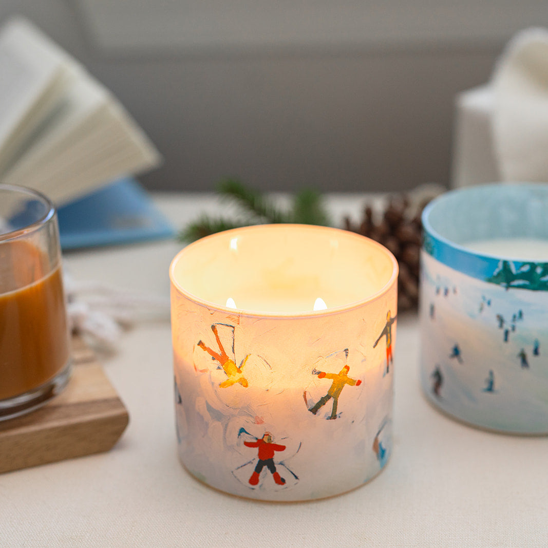 Candle with skiing design on a table with a glass of coffee and decorative items.