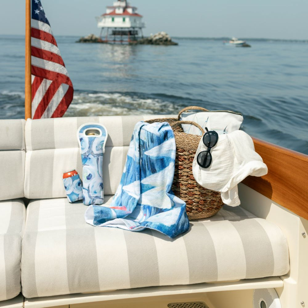 picnic yacht on the water with kim hovell oyster pattern wine tote and koozie beside a sailboat pattern beach towel.