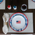 Dining table setting with a plate featuring an American flag, surrounded by placemats and cutlery.