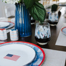 Dining table setting with red, white, and blue nautical plates, glasses, and a vase of flowers.