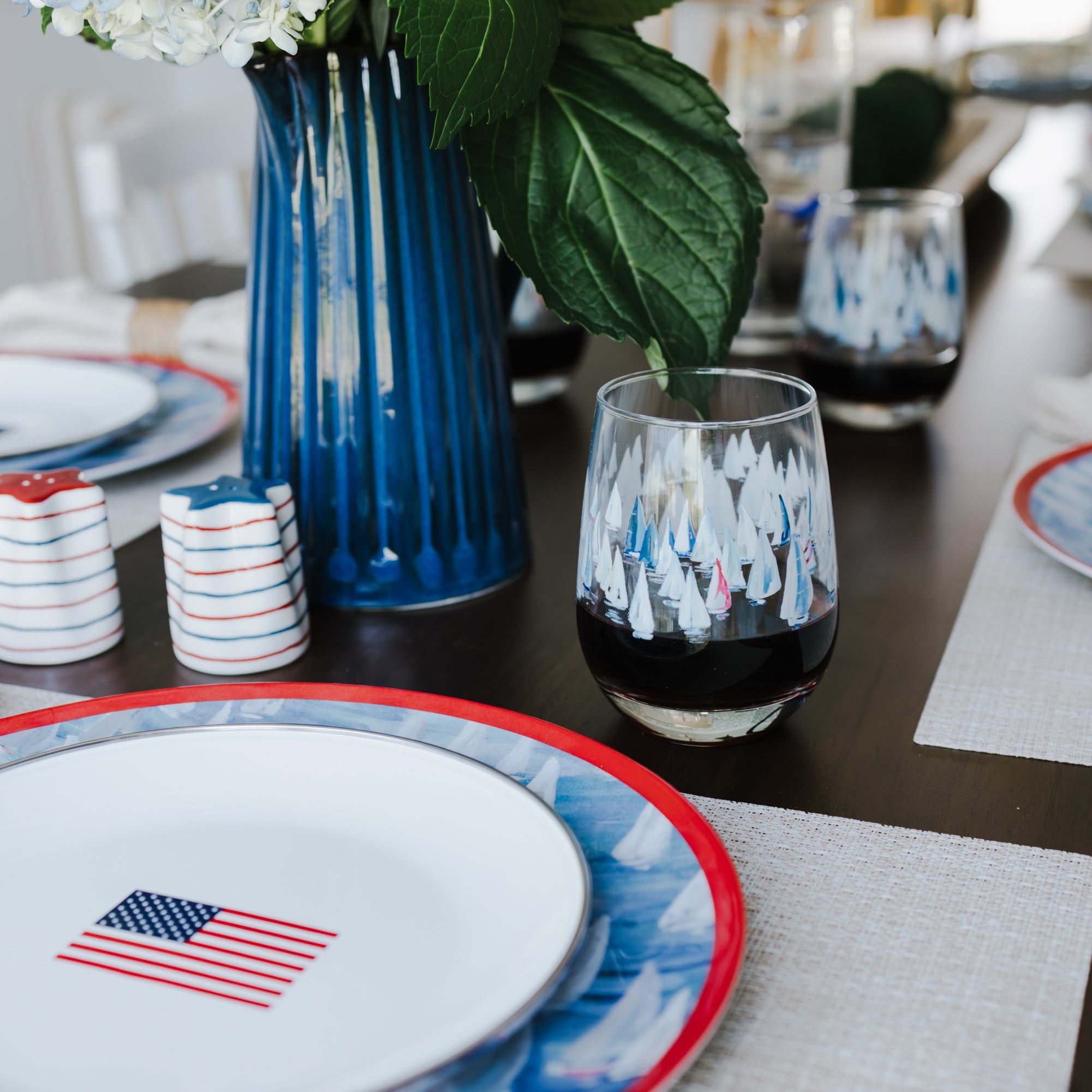 Dining table setting with red, white, and blue nautical plates, glasses, and a vase of flowers.
