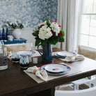 Dining room table set with plates, glasses, and a vase of flowers in a home setting.