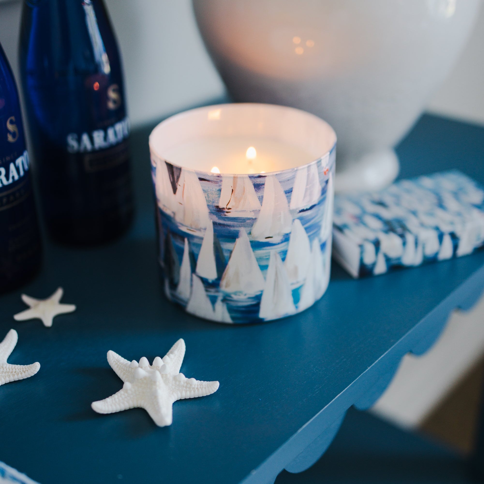 decorative blue and white candle on a blue surface with starfish and a bottle in the background