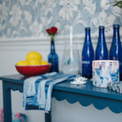 Decorative setting with blue bottles, a white pitcher, and a bowl of fruit on a shelf.