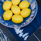 Blue plate with white boat pattern containing yellow lemons on a blue surface.