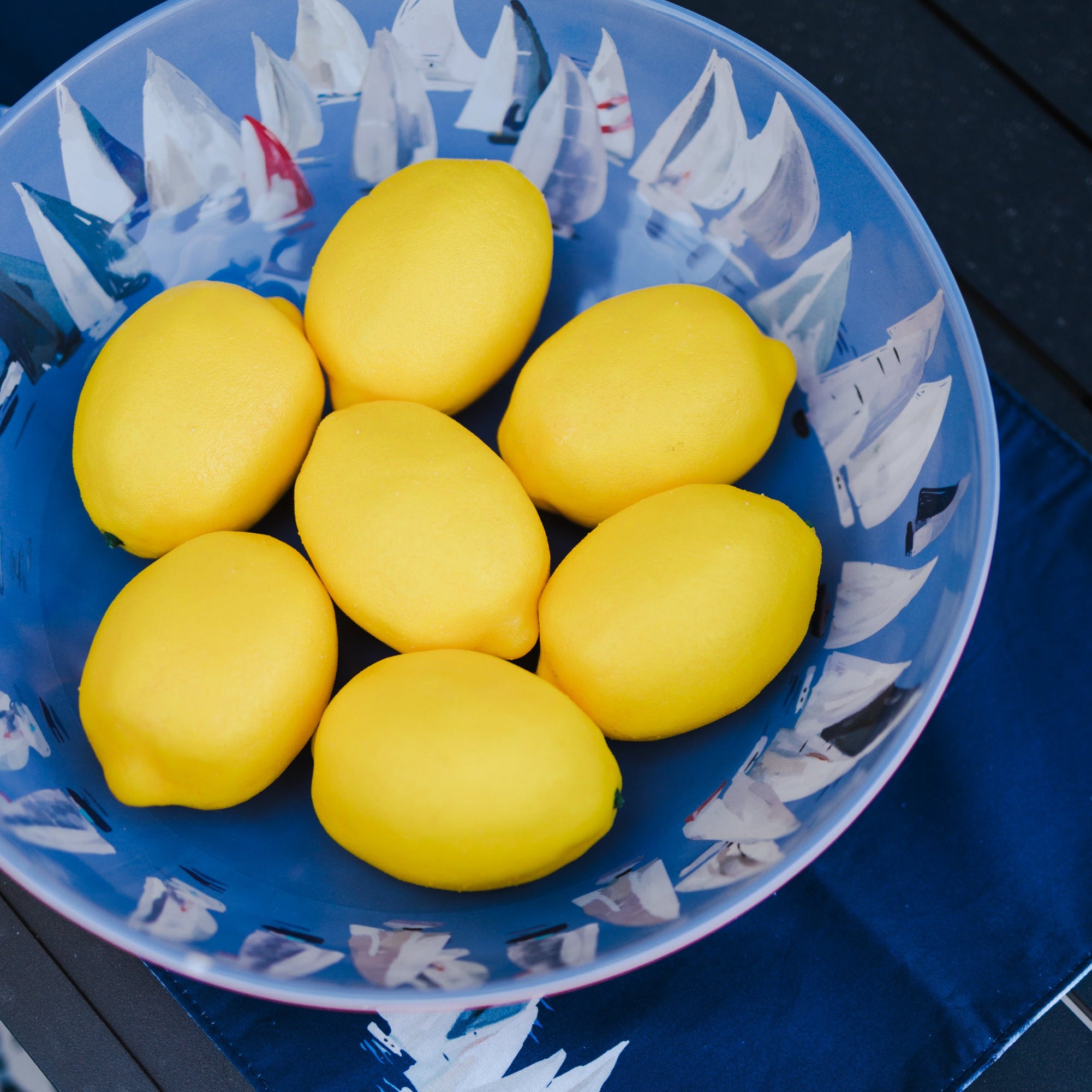 Blue bowl with red outer exterior featuring white boat pattern on interior containing yellow lemons on a blue surface.