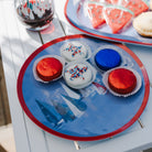 Colorful cupcakes on a blue plate with a glass of red wine on a white table.