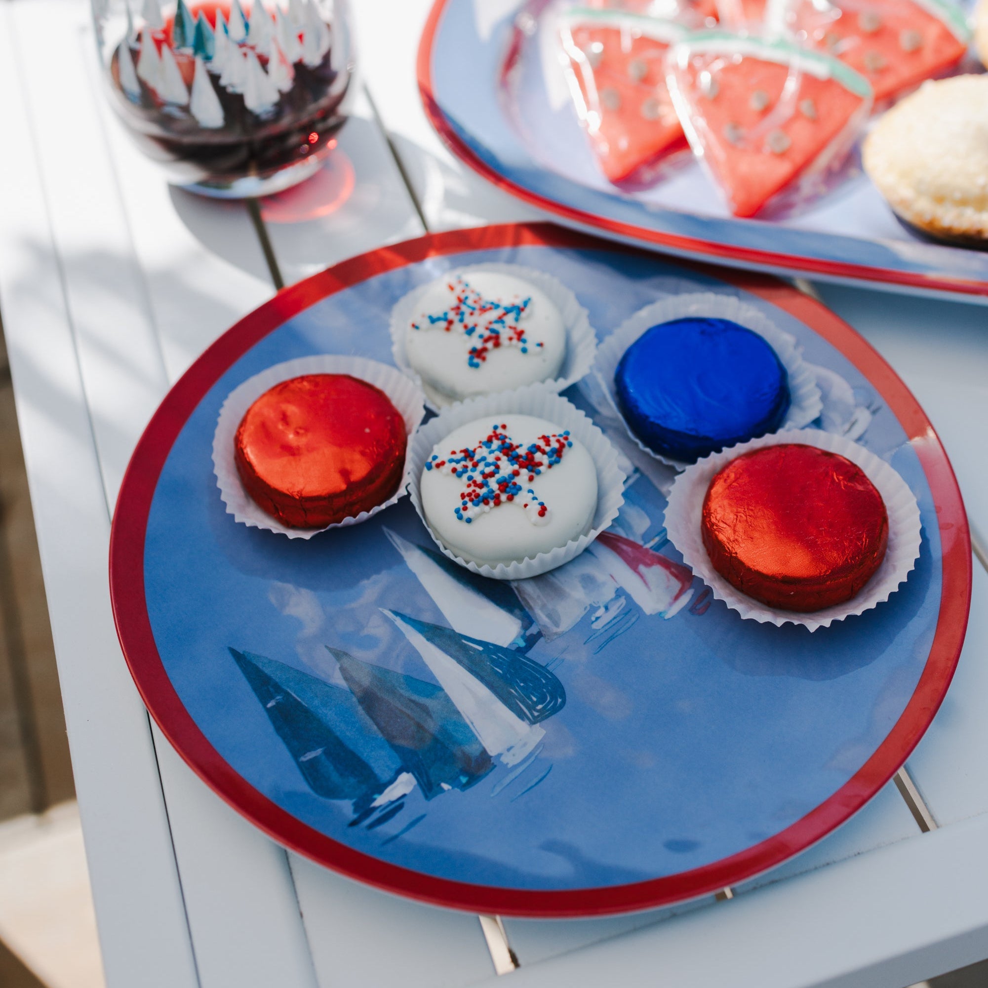 Colorful cupcakes on a blue plate with a glass of red wine on a white table.