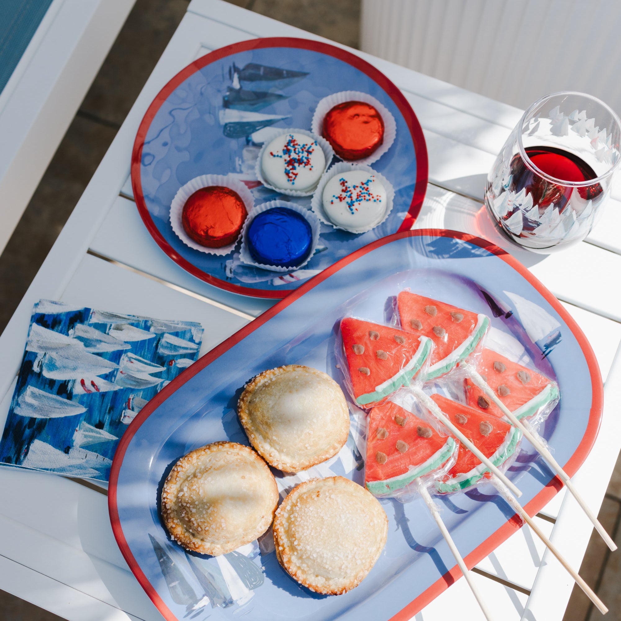 Tray with cookies, watermelon slices on sticks, and small bottles of red and blue liquid on a white surface.