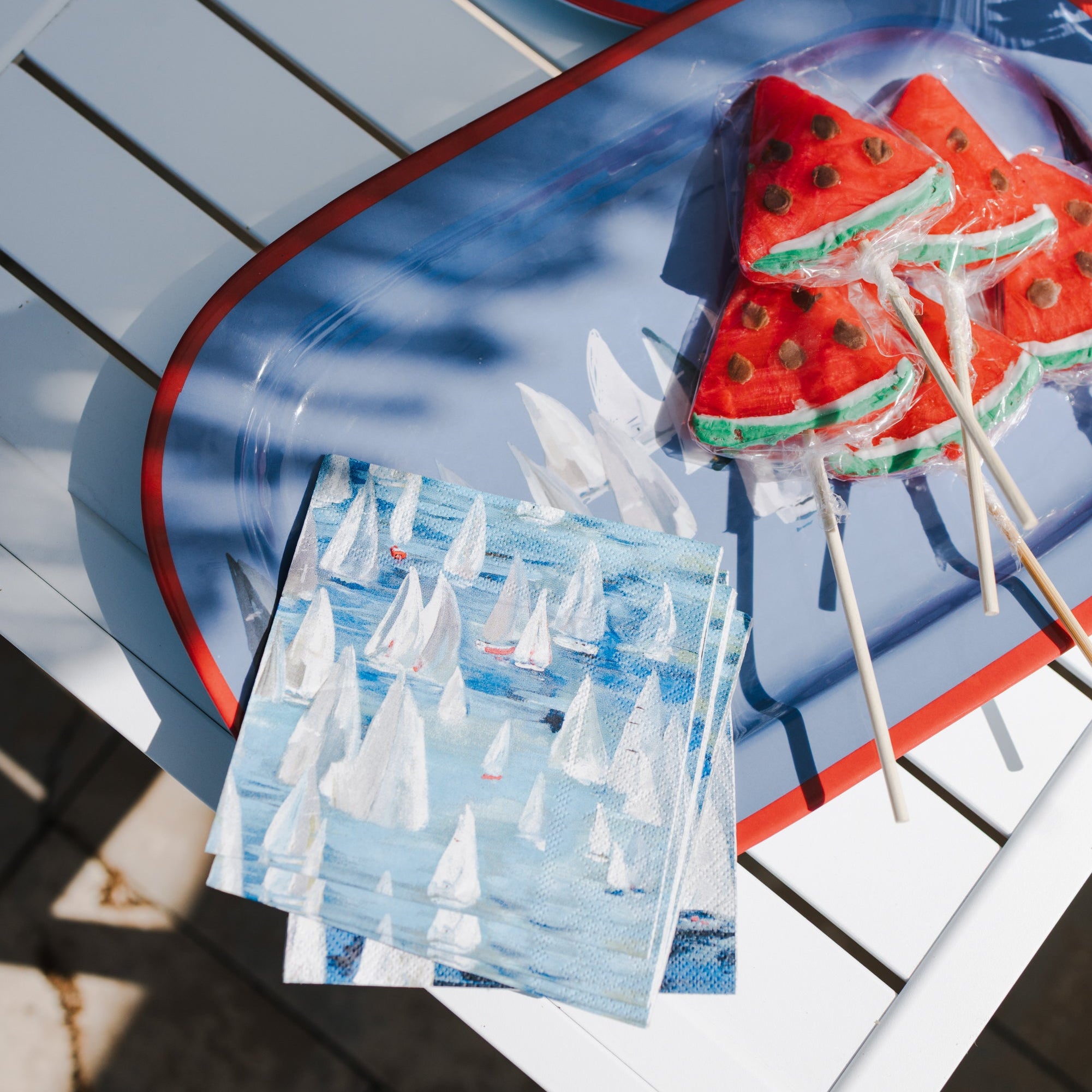 Decorative plates with watermelon-themed lollipops and colorful cupcakes on a wooden surface.