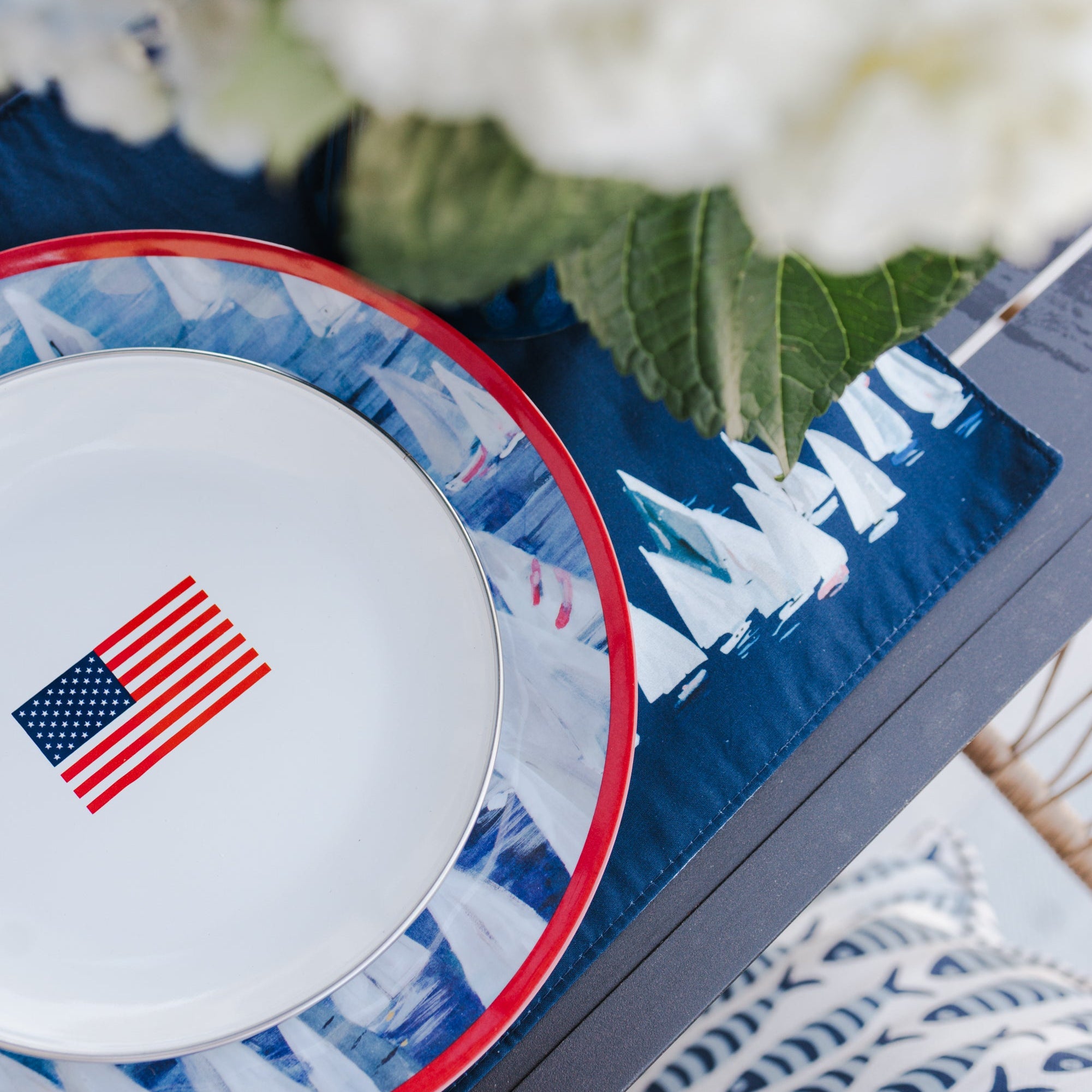 Sailboat table setting with a plate featuring an American flag, surrounded by white hydrangeas.