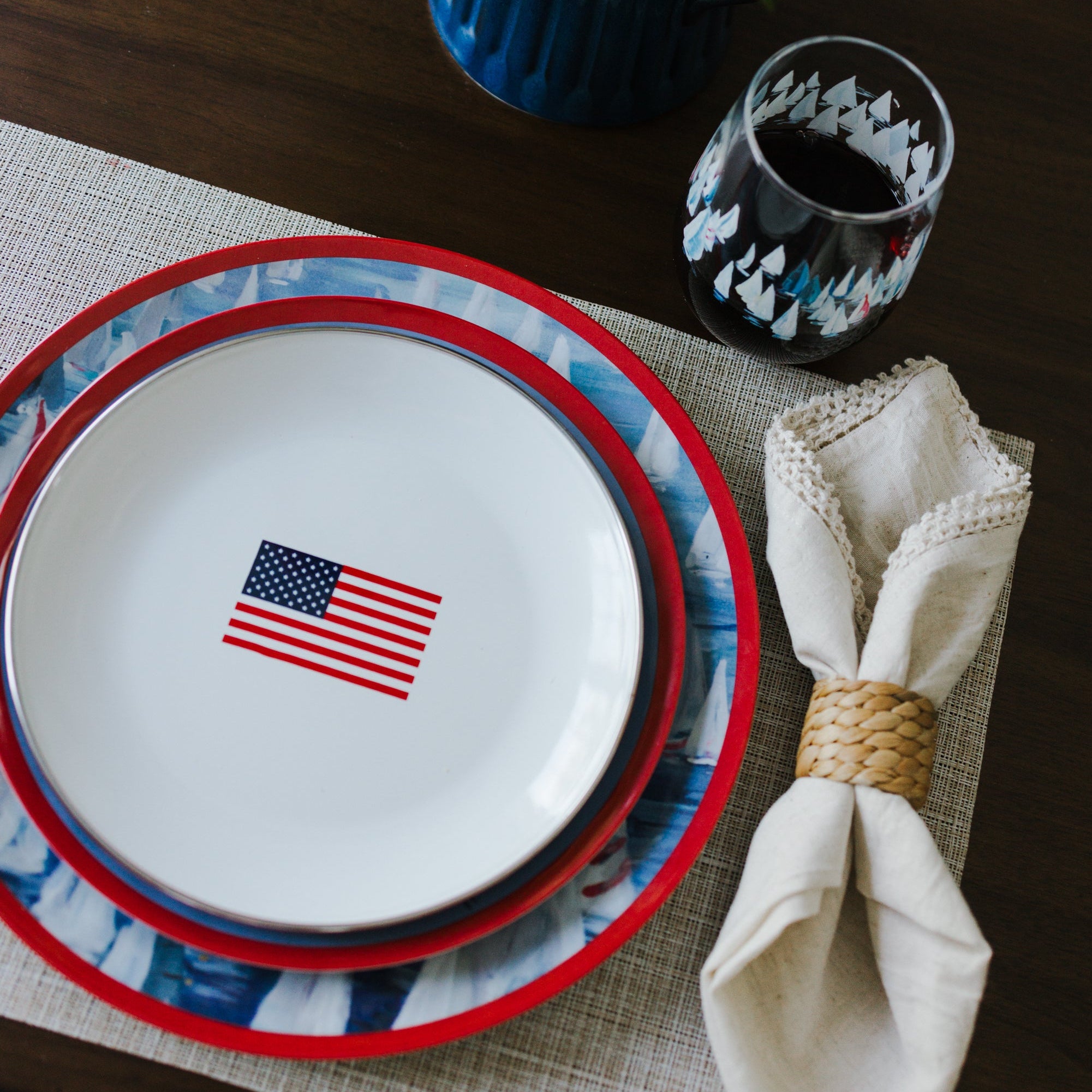 Stack of plates with American flag design on a table setting with a napkin and glass.