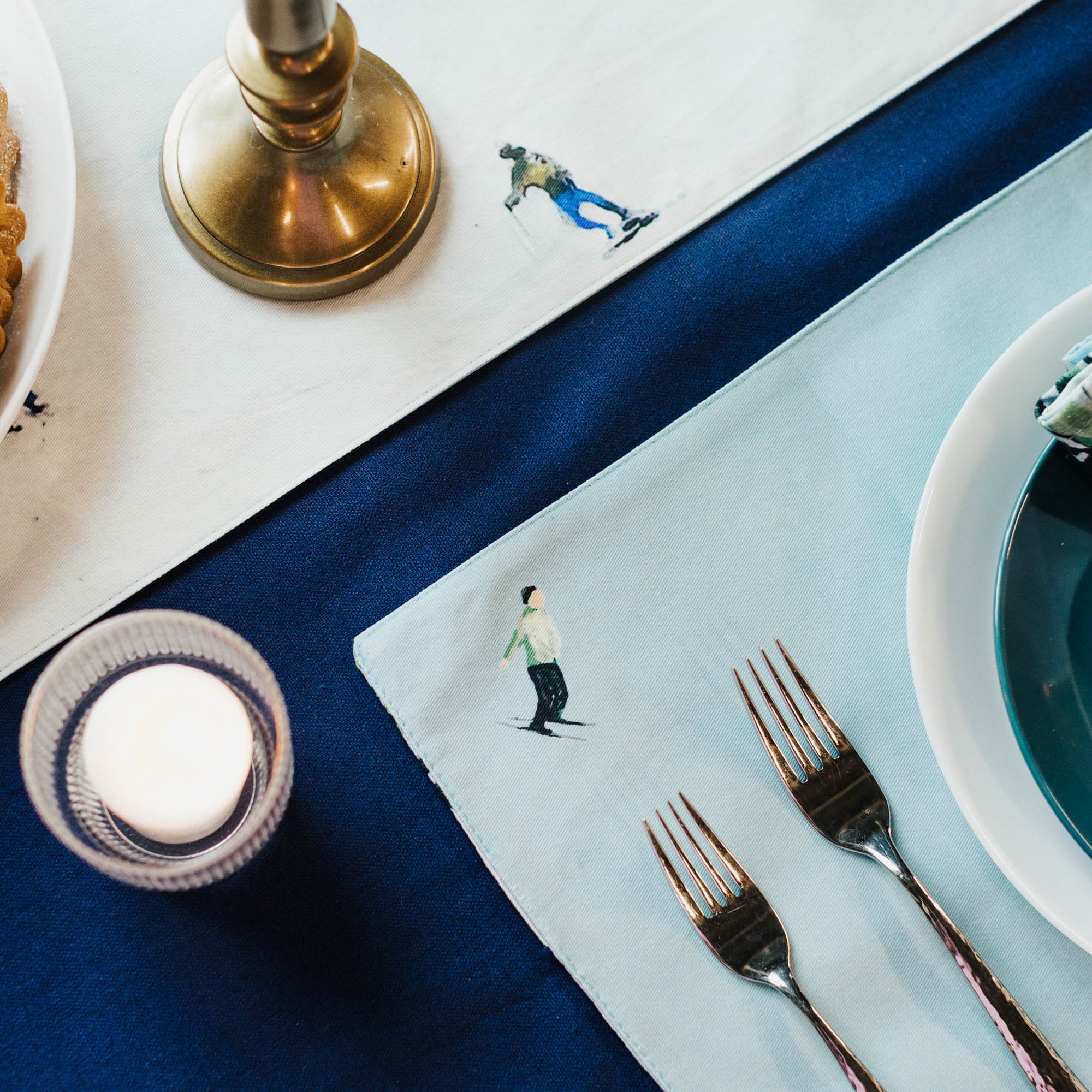 Dining table setting with blue placemats, silverware, and a candle.