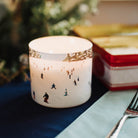 Candle with decorative design on a table with a fork and Christmas decorations.
