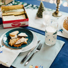 Christmas-themed table setting with cookies, holiday theme glass, and a candle.