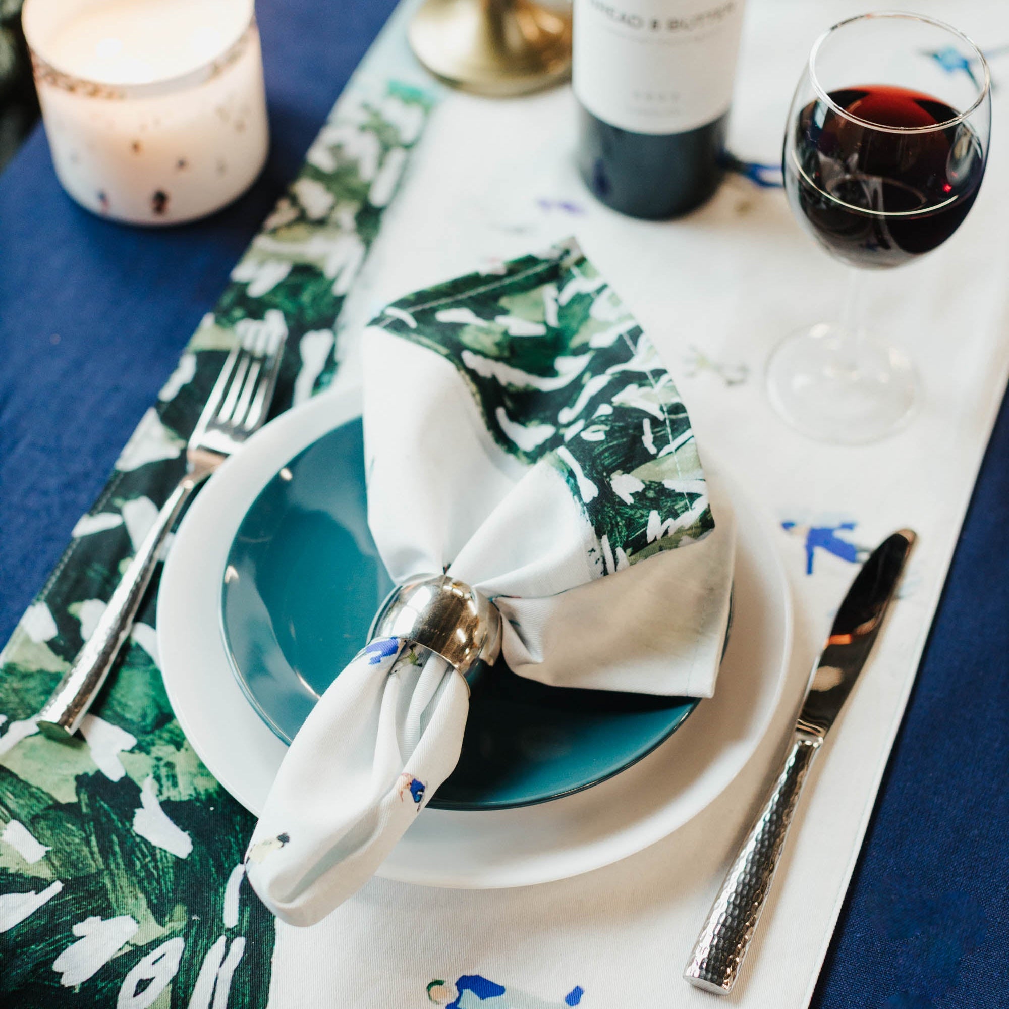 Elegant table setting with wine, plates, and cutlery on a decorative tablecloth.