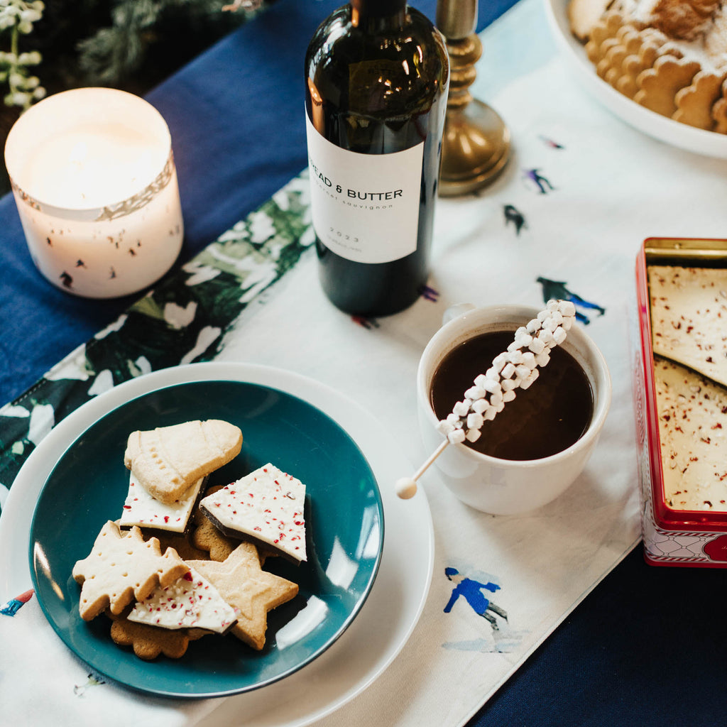 Table setting with cookies, wine, and hot chocolate on a decorative ski tablecloth.
