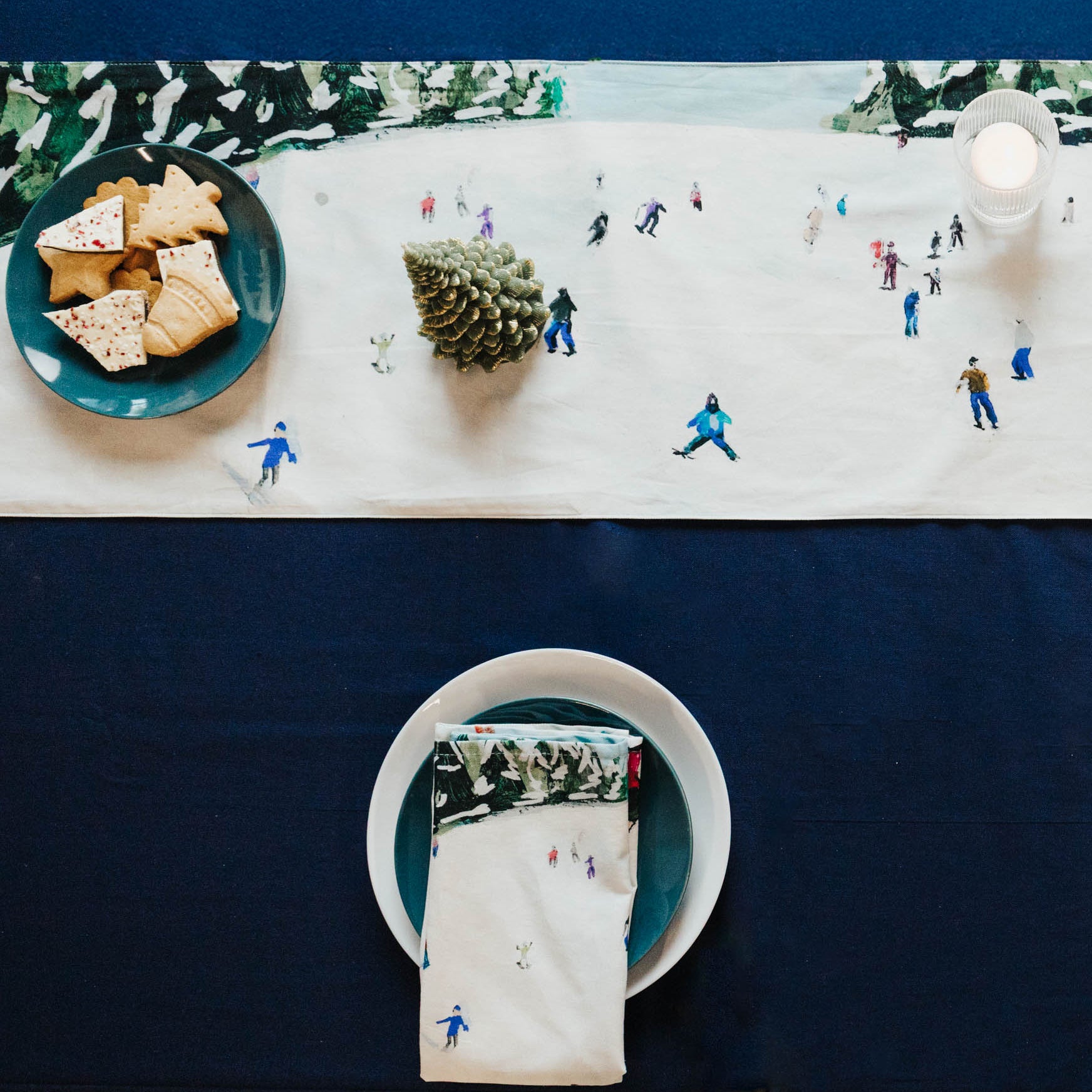 Table setting with miniature skiers on a snowy scene tablecloth against a blue background