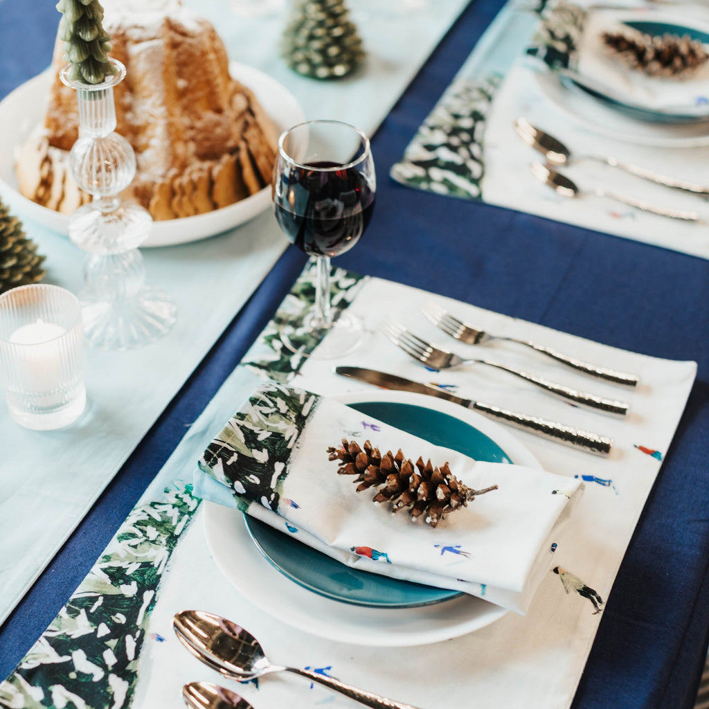 Elegant Christmas table setting with blue tablecloth, decorative placemats, and festive decor.