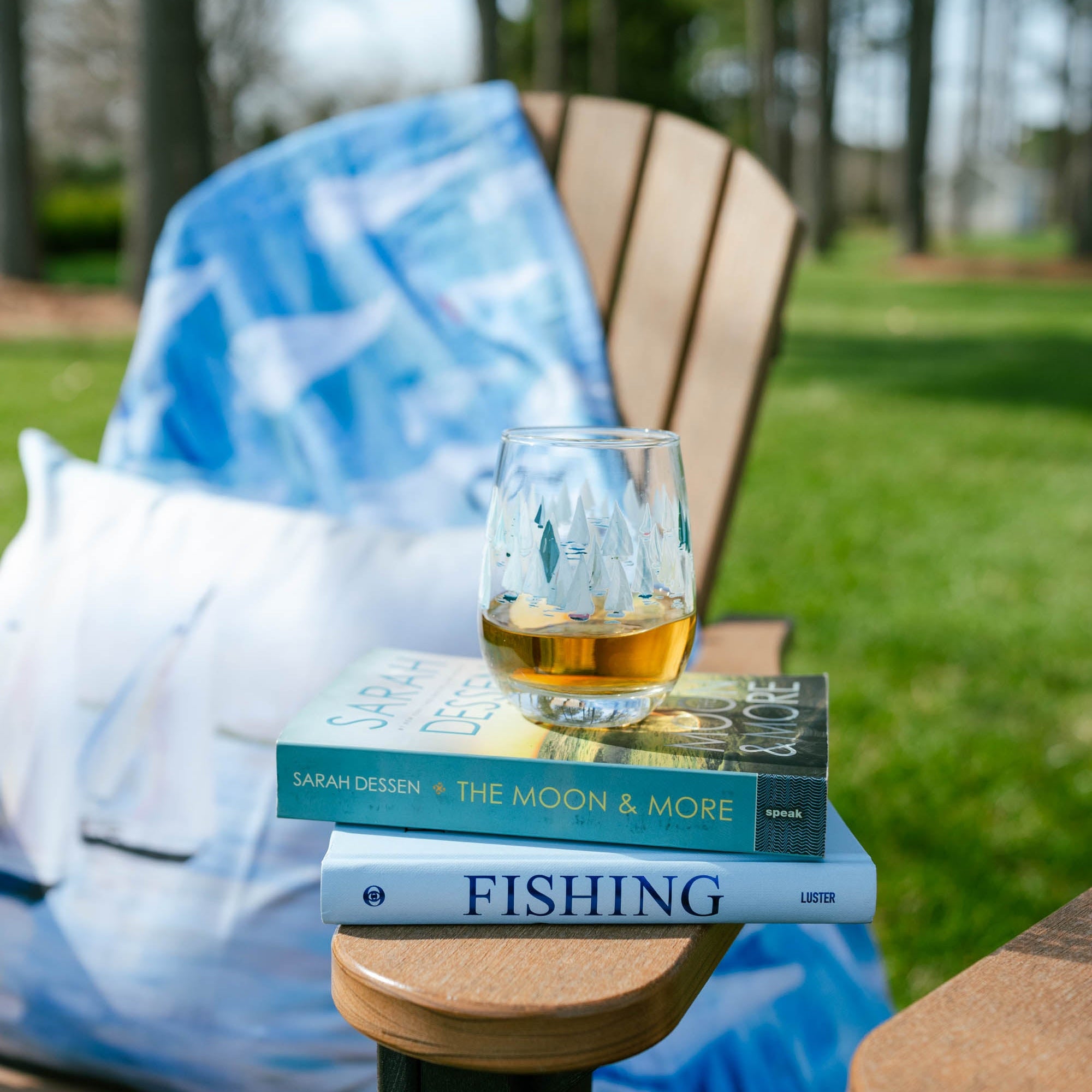 Fishing books with a glass of whiskey on a table outdoors