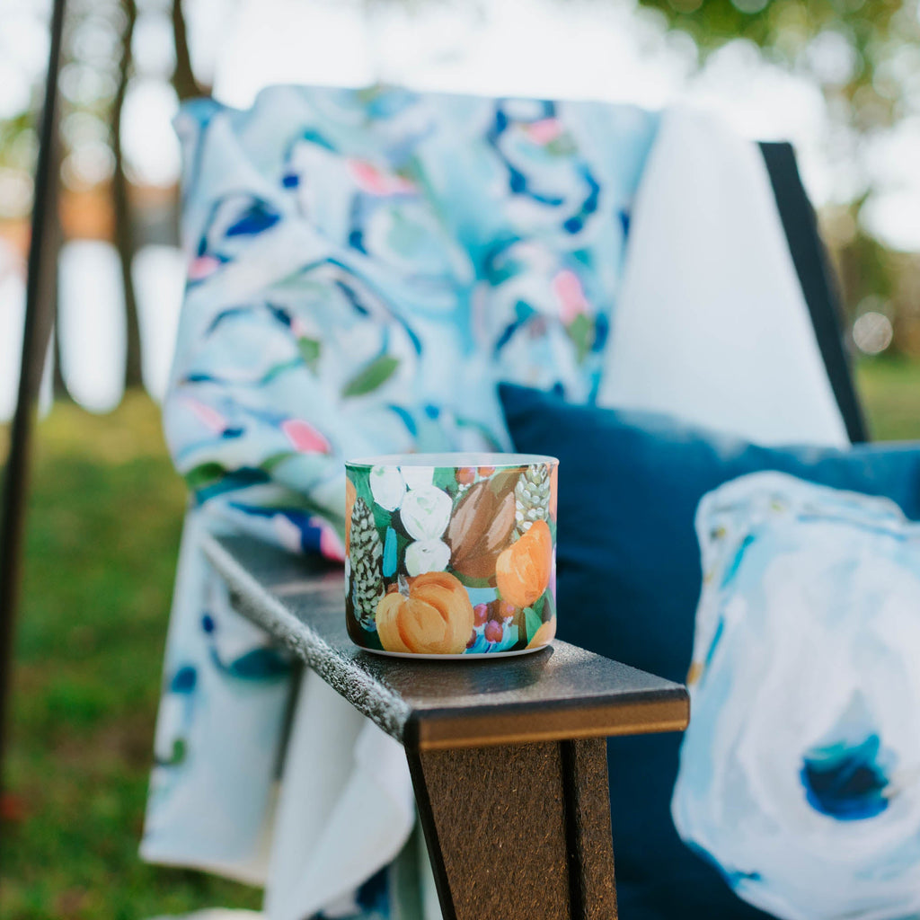 Festive fall candle on a table with decorative pillows in an outdoor setting