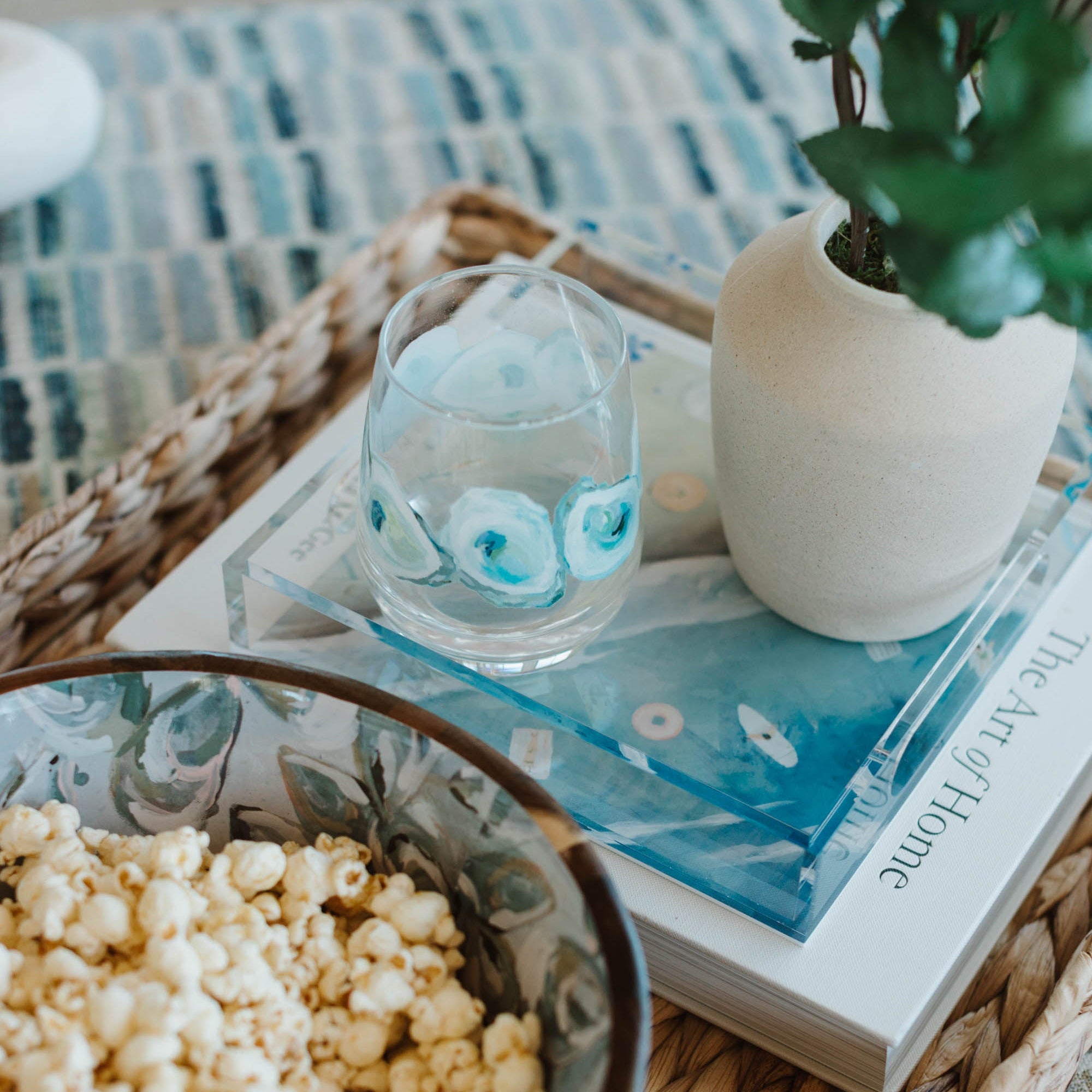 Bowl of popcorn on a woven tray with a book and decorative items.