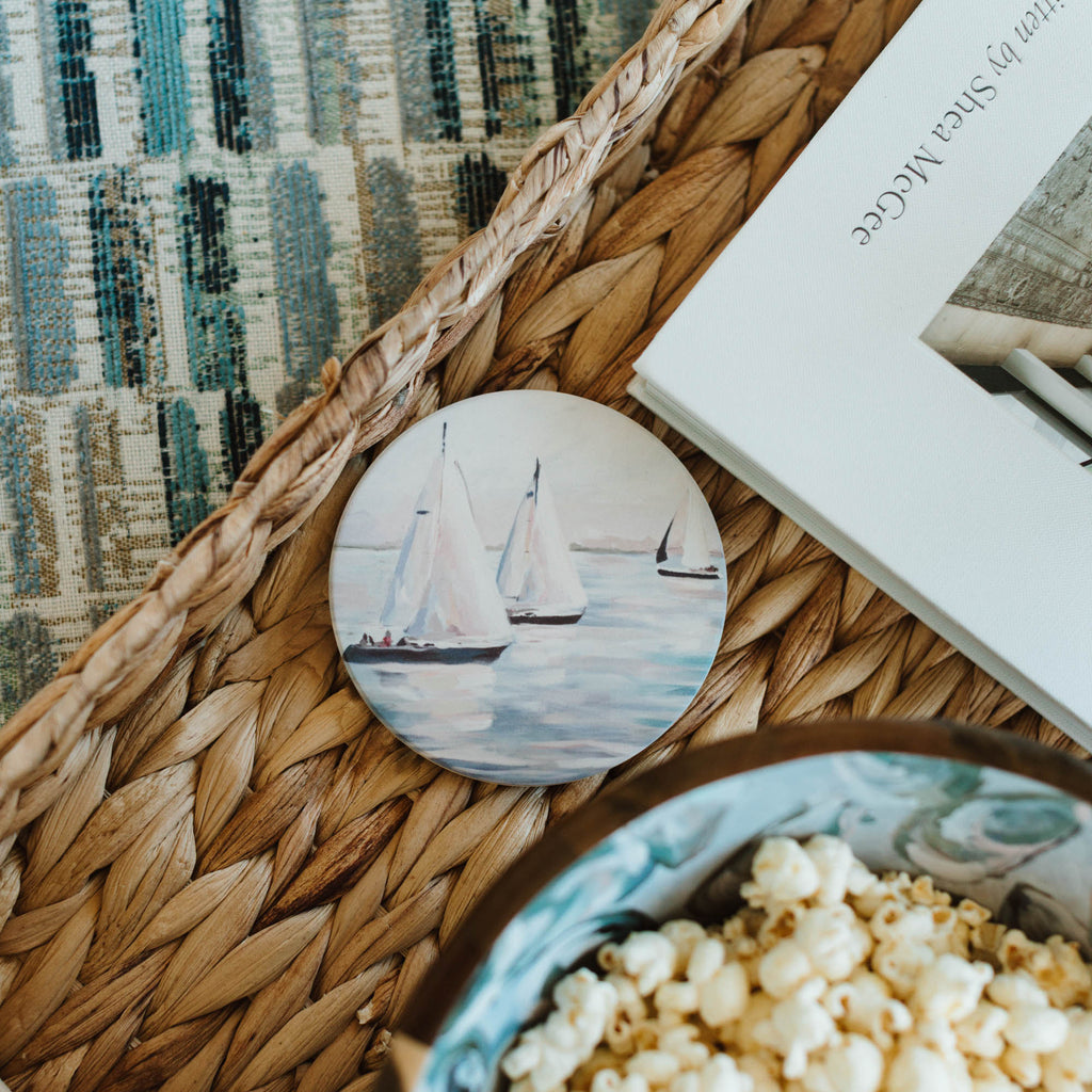 Coaster with sailboat design on a woven surface with popcorn and book