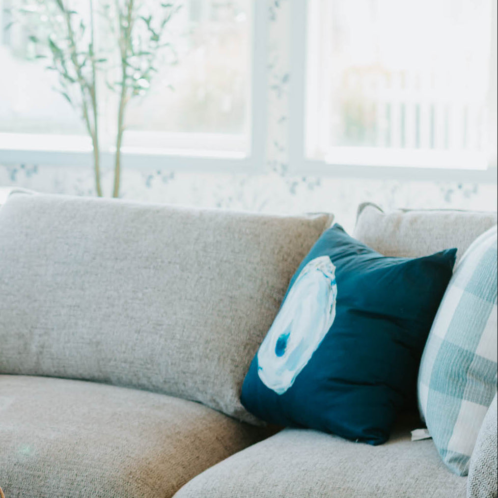 Living room with a beige sectional sofa, patterned ottoman, and decorative pillows.