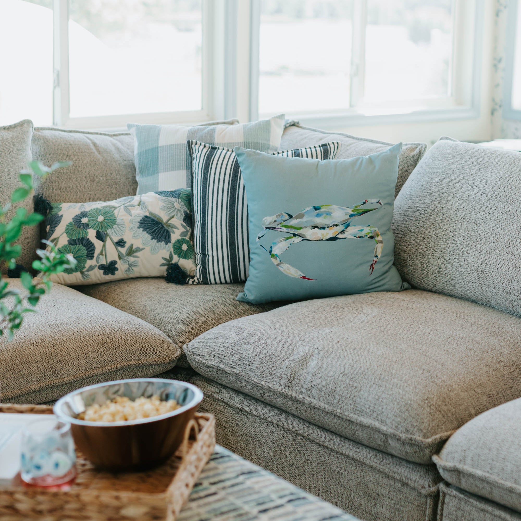 Gray sectional sofa with decorative pillows in a bright room with large windows.