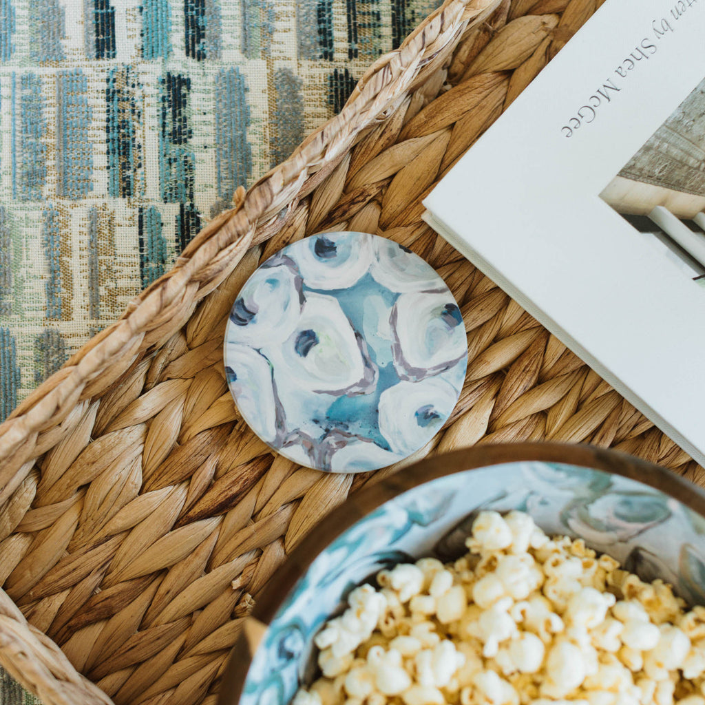 Kim Hovell sandstone coaster with oyster design on a woven tray with popcorn and a book.