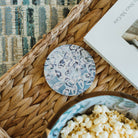 Bowl of popcorn on a woven mat with decorative coaster and book