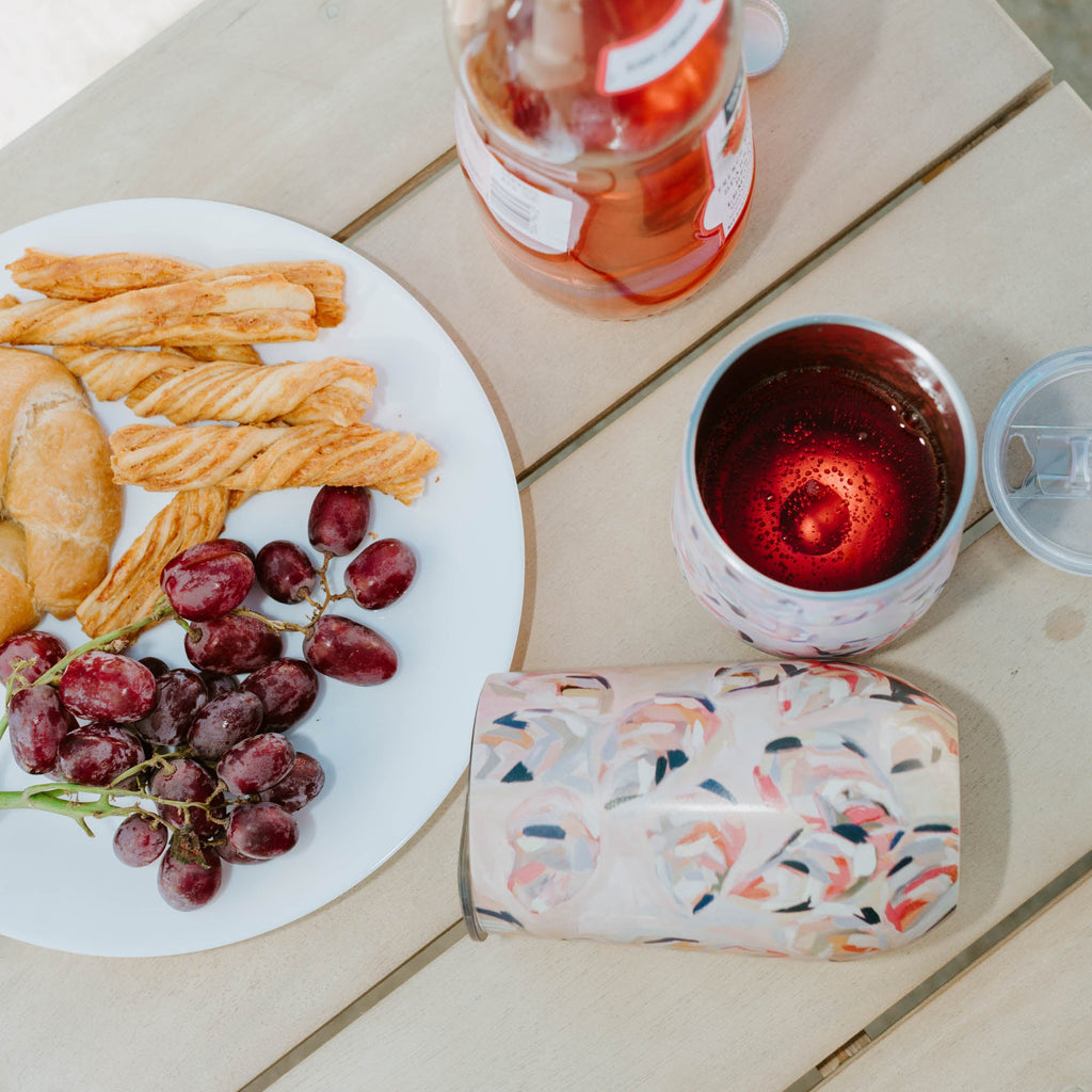 Bottle of rosé, plate with snacks, and pink wine tumbler on a wooden surface