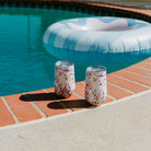 Two Kim Hovell Peach Gems shell-patterned wine tumblers on a poolside ledge with an inflatable pool toy in the background.