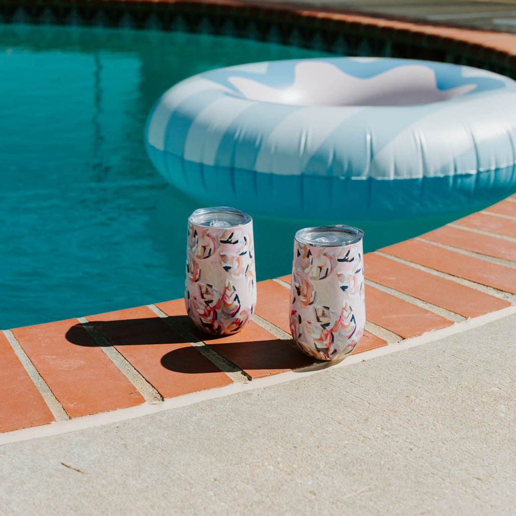 Two shell-patterned cups on a poolside ledge with an inflatable pool toy in the background.