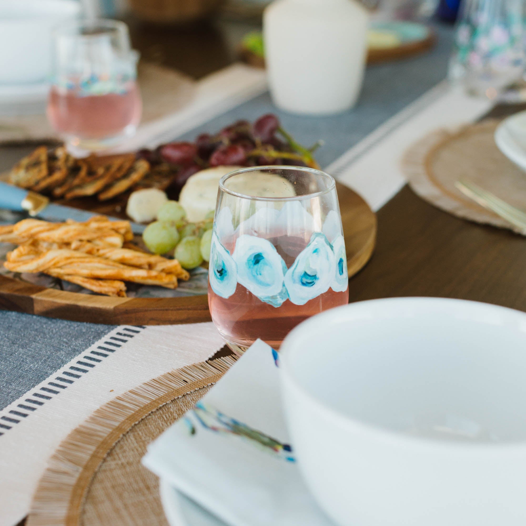 Dining table setting with kim hovell oyster pattern wine glasses, plates, and appetizers on a textured surface.