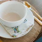 White ceramic bowl on a woven placemat with a crab-pattern napkin and gold spoon.