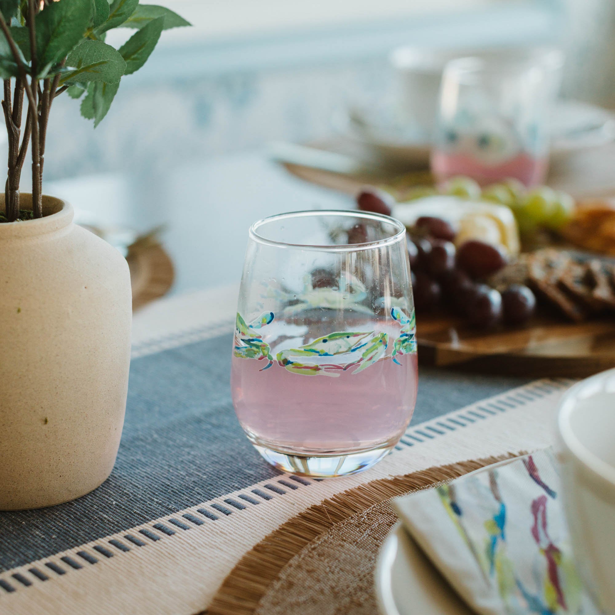 Glass of pink lemonade on a table with a plant and fruit plate in the background