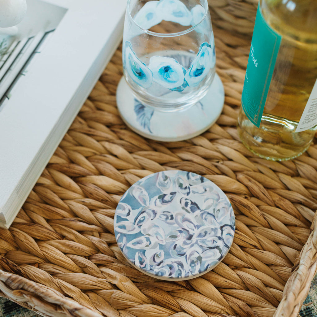 Decorative glass coaster with blue floral design on a woven tray with a book and bottle.
