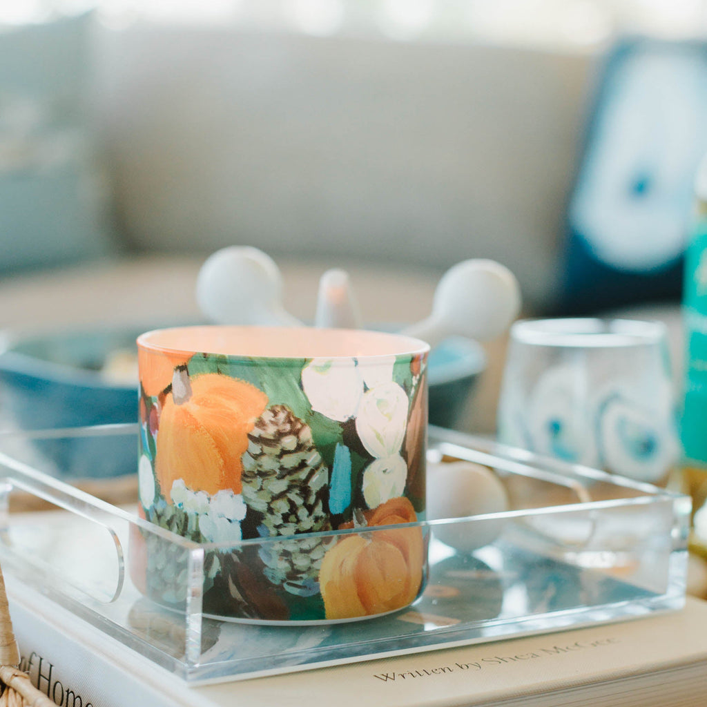 Decorative fall candle with pumpkins and pinecones on a book in a cozy living room setting.