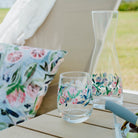 Outdoor setting with floral glasses and carafe on a table, blurred background