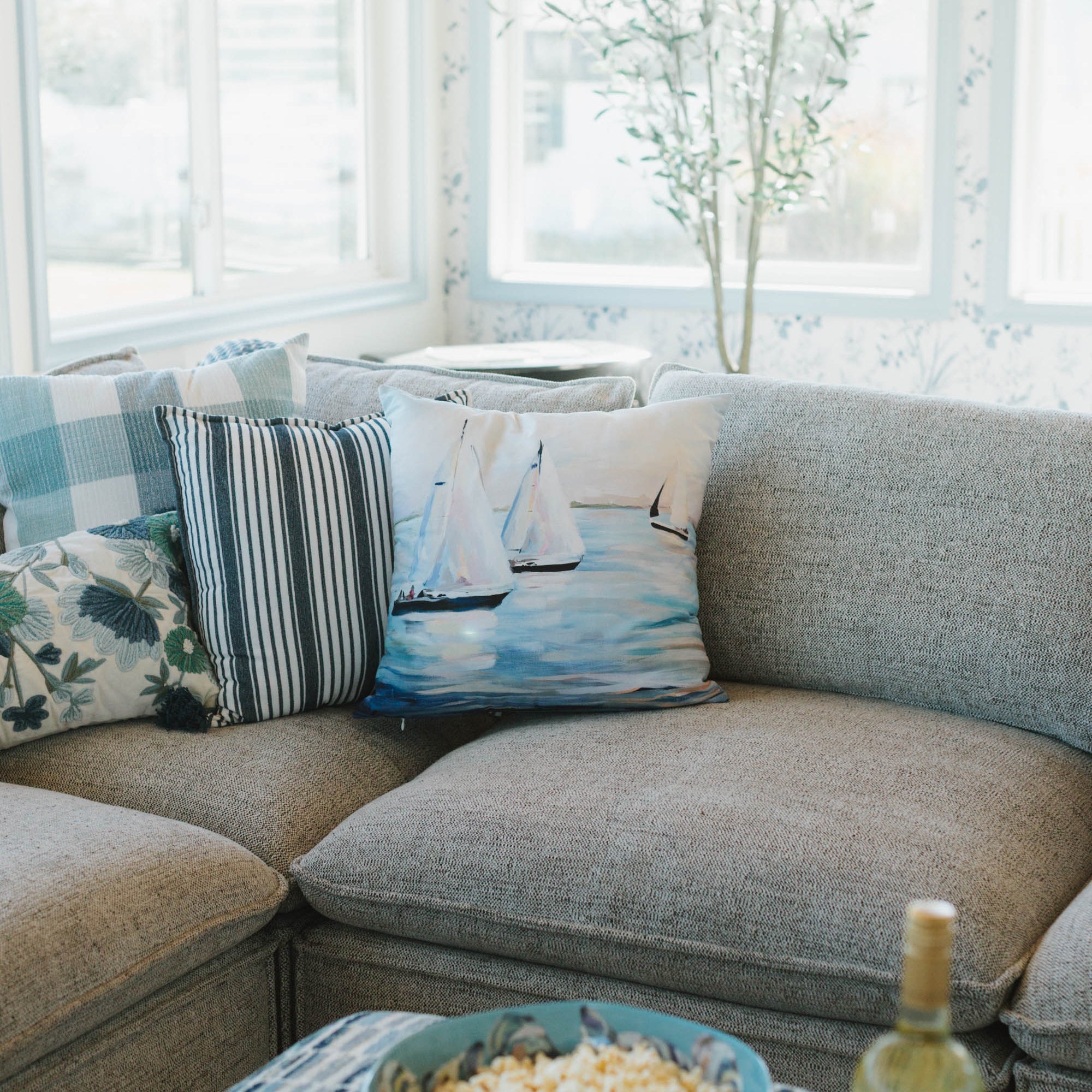 Living room with a sectional sofa, sailboat pillows, a bowl of popcorn, and a bottle of wine.