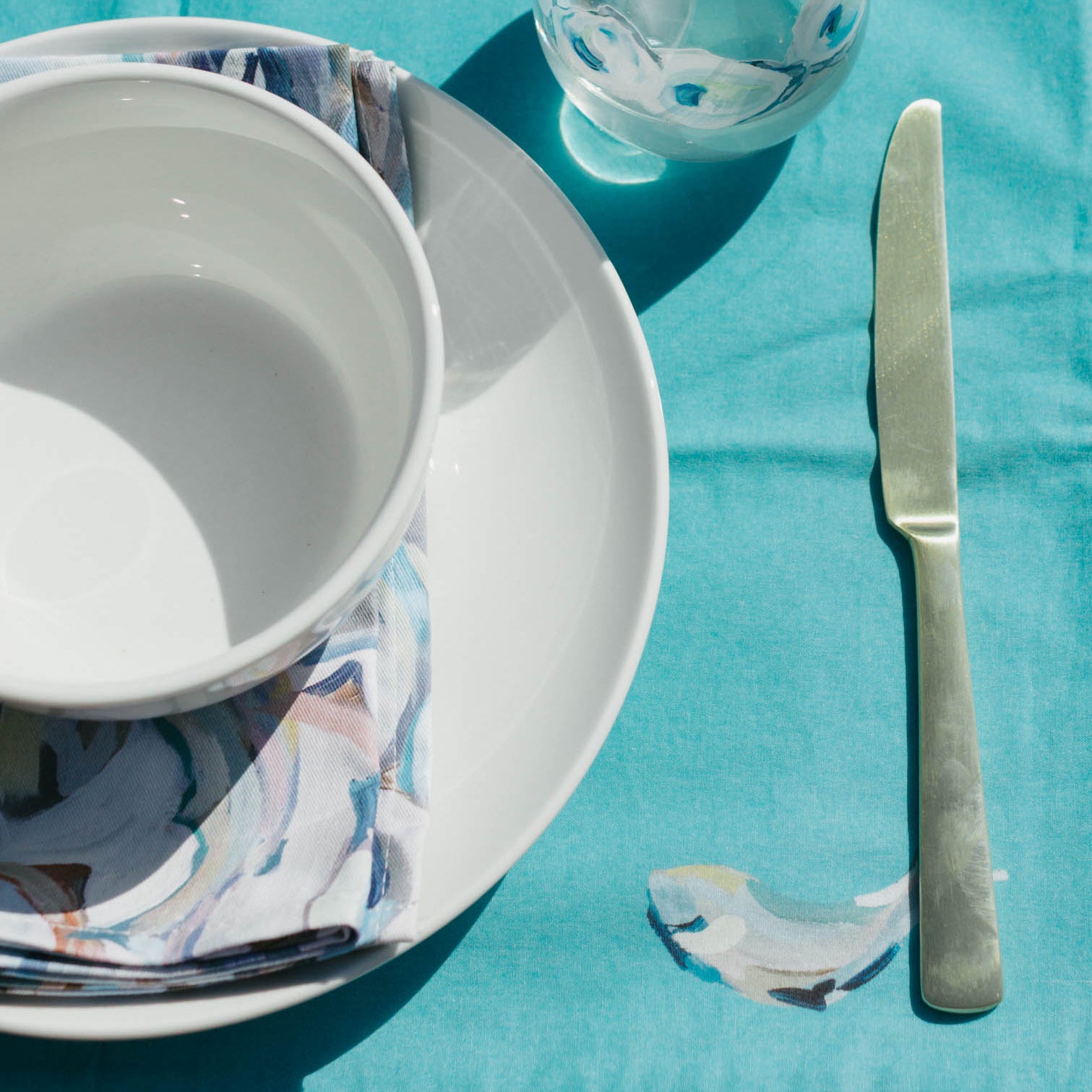 Table setting with blue placemats, white bowls, silverware, and a glass of water on a dark wooden table.
