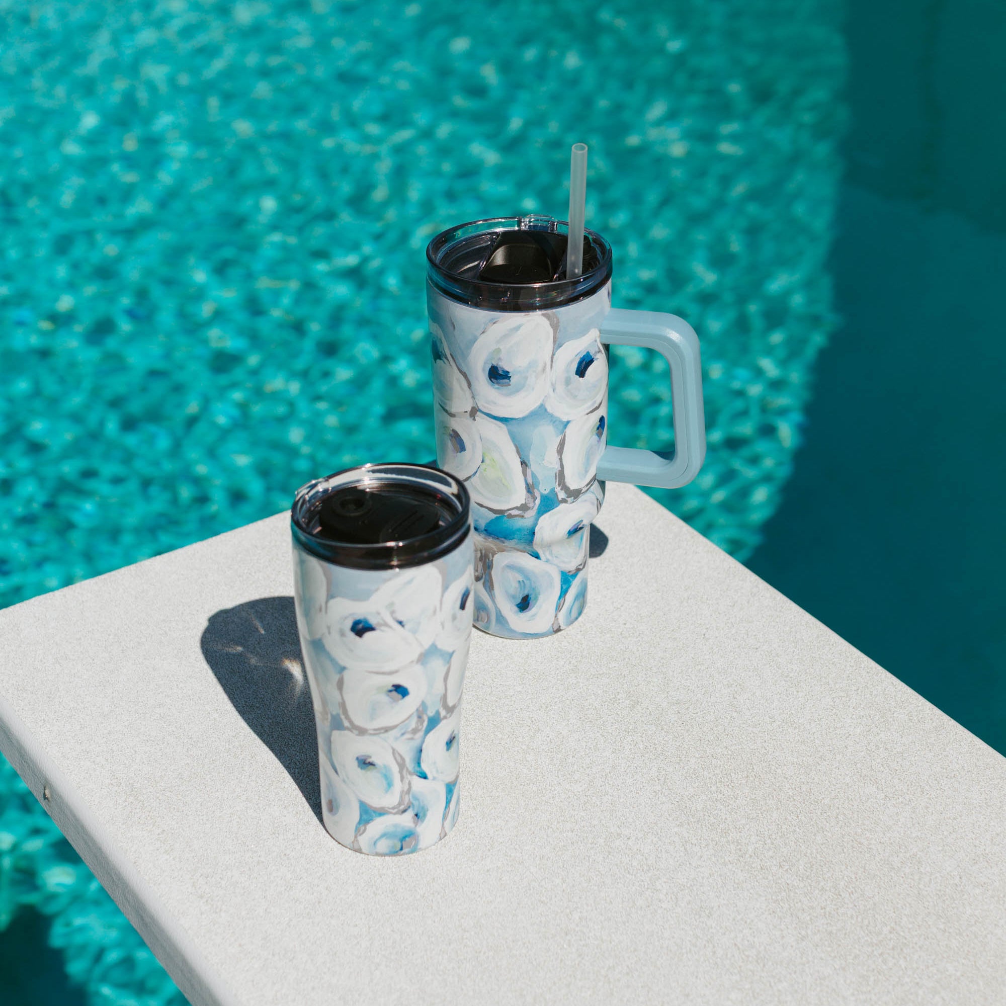 A blue and white oyster patterned 20oz and 40oz tumbler with removable lids, displaying the 'Ebb and Flow' artwork on a pool diving board.