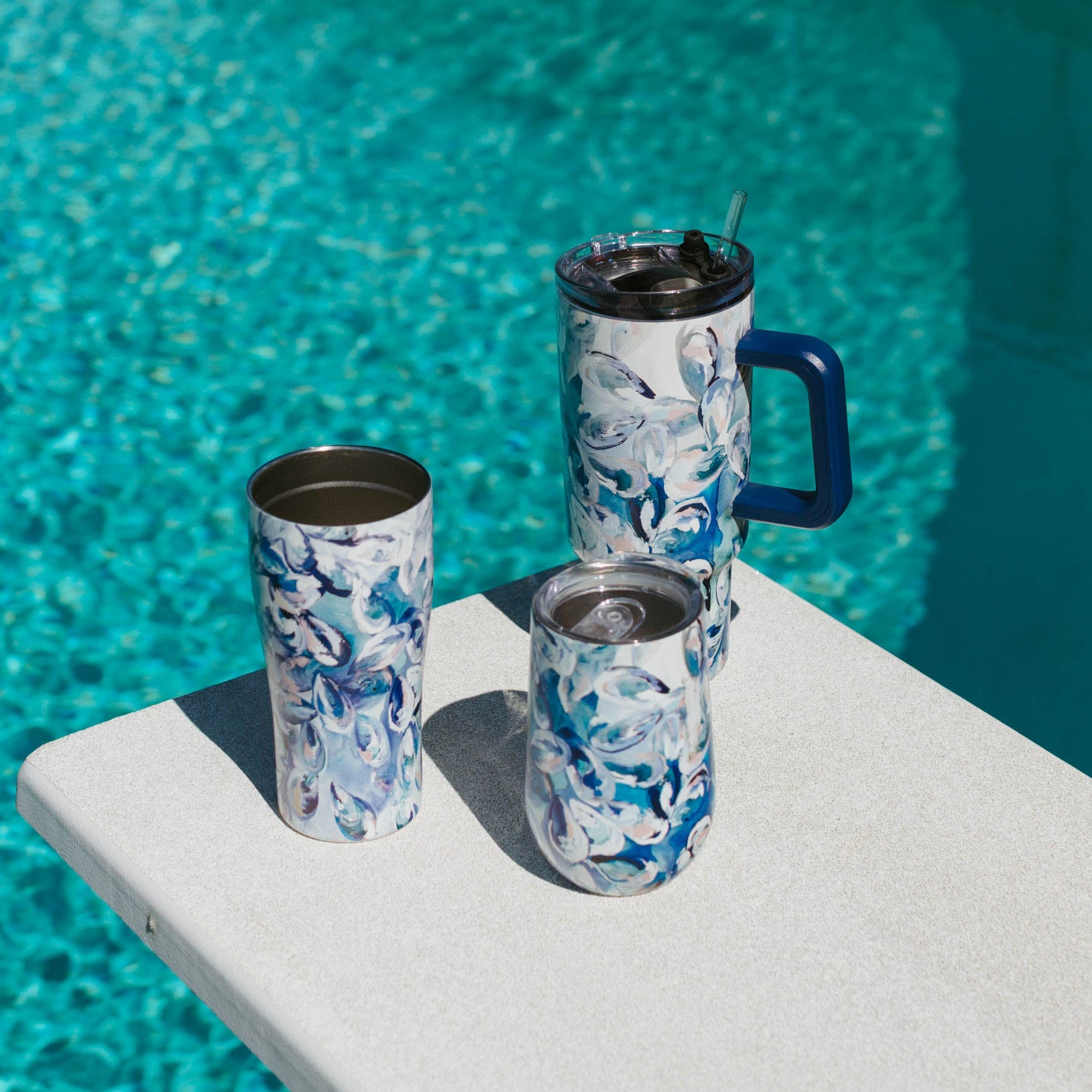 Three insulated Kim Hovell tumbler sizes with blue shell pattern 'Azul Oysters' on a pool diving board