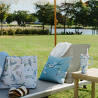 Outdoor setting with lounge chair, cushions, and a table by a lake.
