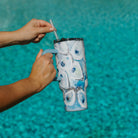 Person holding a tumbler with a blue and white oyster design against a blurred pool background
